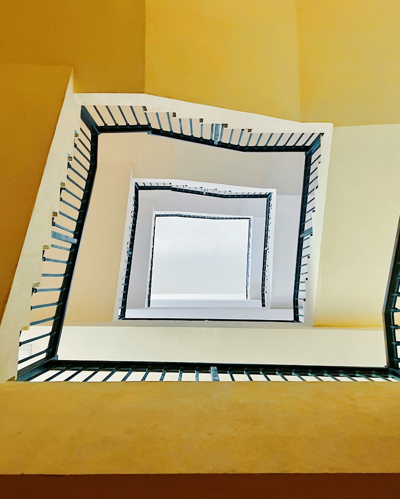 Looking up through the open stair of a pale building