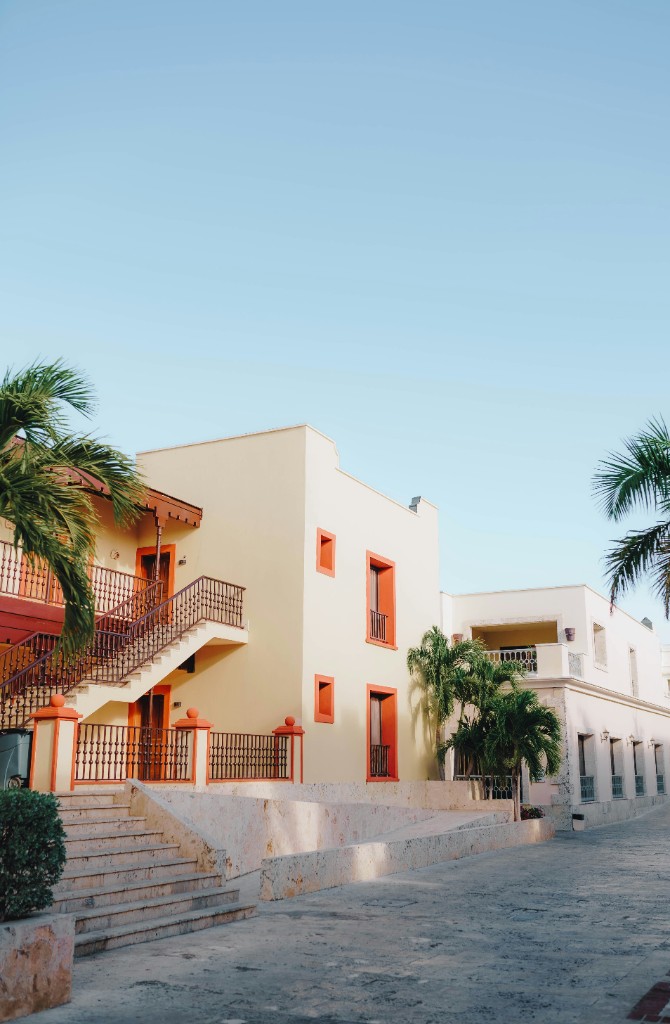 A cream house with terracotta trim, palms, and an outside stair